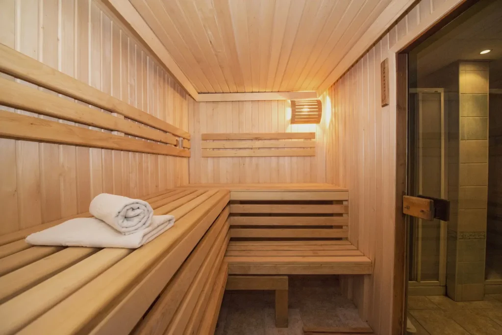 "Interior of a traditional wooden sauna with bench seating, warm lighting, and a folded towel placed on one of the benches."