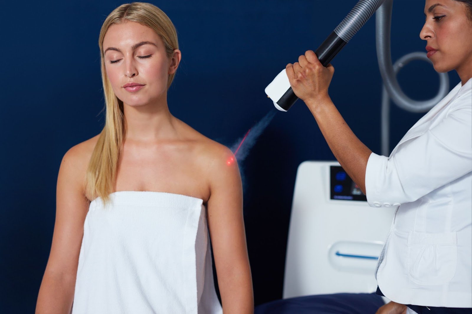 A practitioner aims a handheld transdermal ozone therapy device at a seated woman's shoulder.